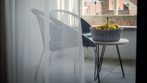 A balcony with a wicker basket containing fruits, a white chair, and a view of buildings in the background. - Pegard Andenne Centre (Andenne)