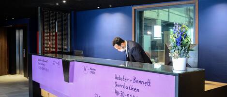 A reception desk with a purple sign, a potted plant, and a glass partition.