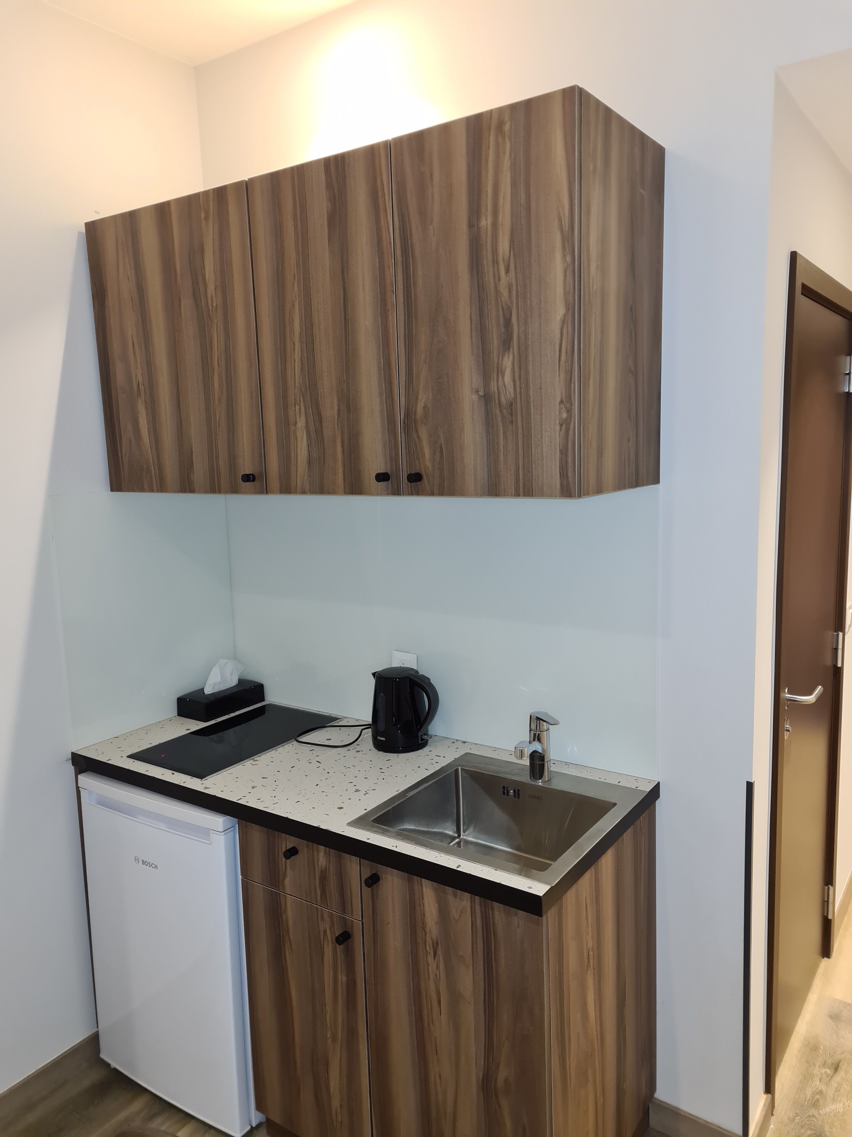 A compact kitchen with wooden cabinets, a Bosch dishwasher, a coffee maker, and a sink.