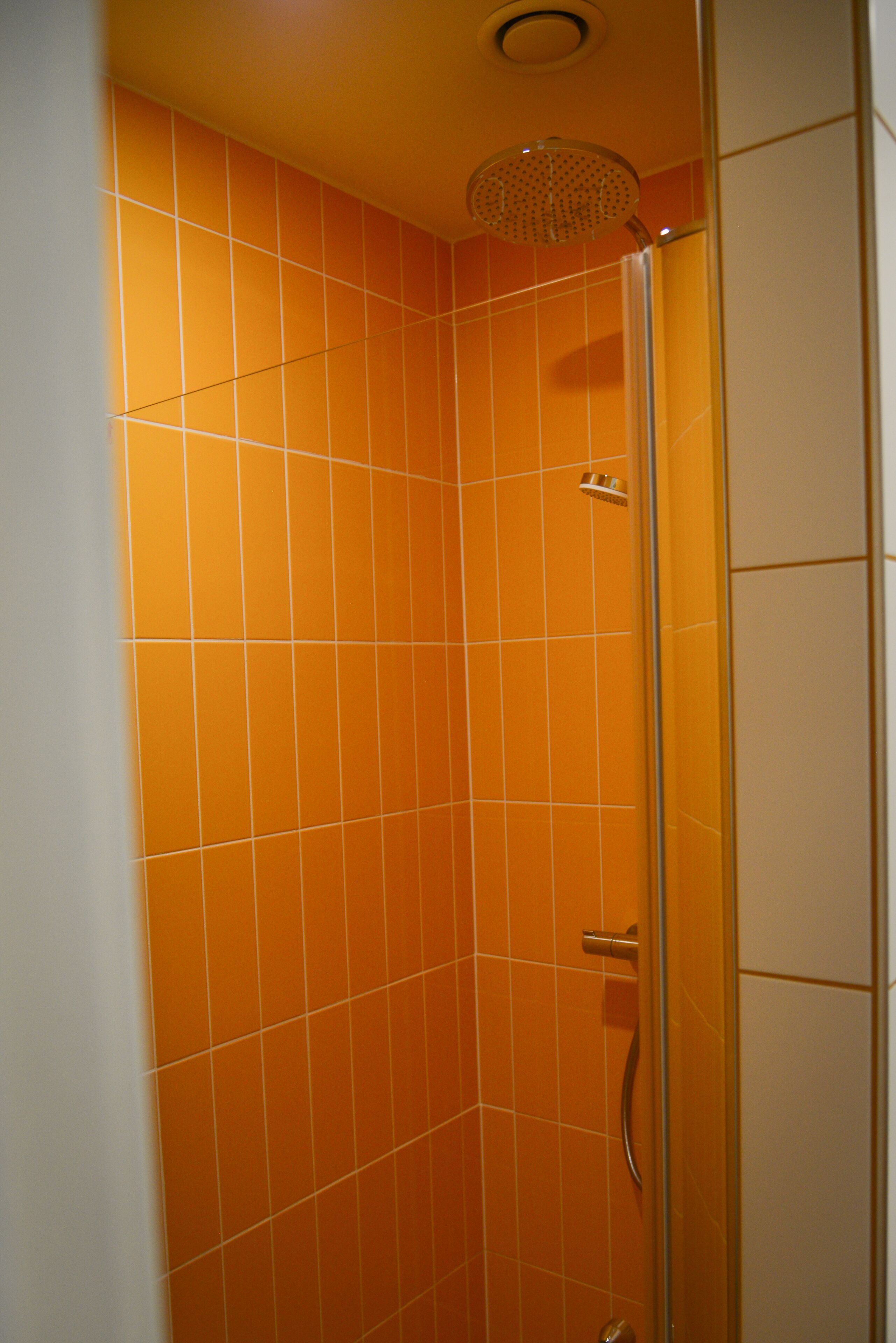A shower with orange tiles and a glass door.