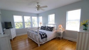 A bedroom with a bed, a ceiling fan, a nightstand, a lamp, a dresser, and a window with blinds. - Oceanview cottage steps to beach access and close to Marina, BHI (Bald Head Island)