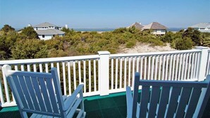 A balcony with white railings and blue chairs overlooking a beach with houses in the background. - Oceanview cottage steps to beach access and close to Marina, BHI (Bald Head Island)