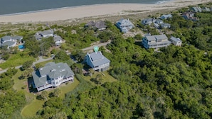 An aerial view of a coastal residential area with houses, a beach, and a body of water. - Oceanview cottage steps to beach access and close to Marina, BHI (Bald Head Island)