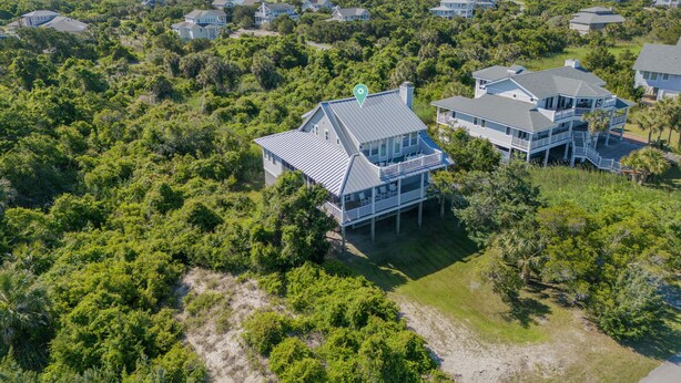 An aerial view of a coastal residential area with multiple houses, dense greenery, and a clear view of the ocean. - Oceanview cottage steps to beach access and close to Marina, BHI (Bald Head Island)