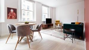 Uma sala de estar moderna com área de jantar, janelas amplas, uma televisão e um sofá verde.