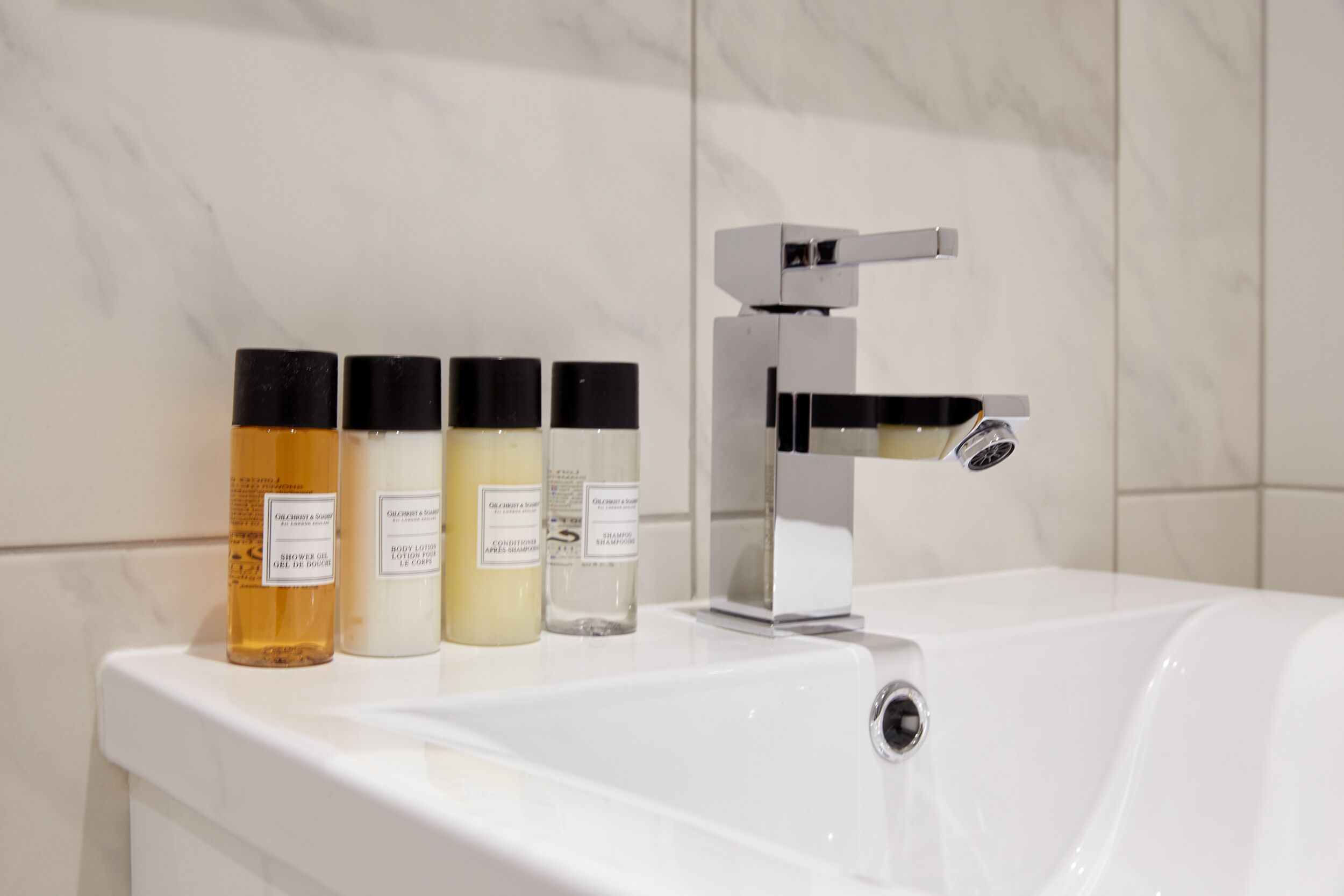 A bathroom with a white sink, four bottles of toiletries, and a modern faucet.