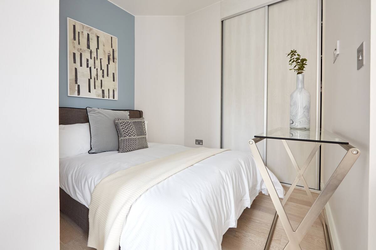 Ein Schlafzimmer mit Bett, Nachttisch, Wandbild und einer Schiebetür.