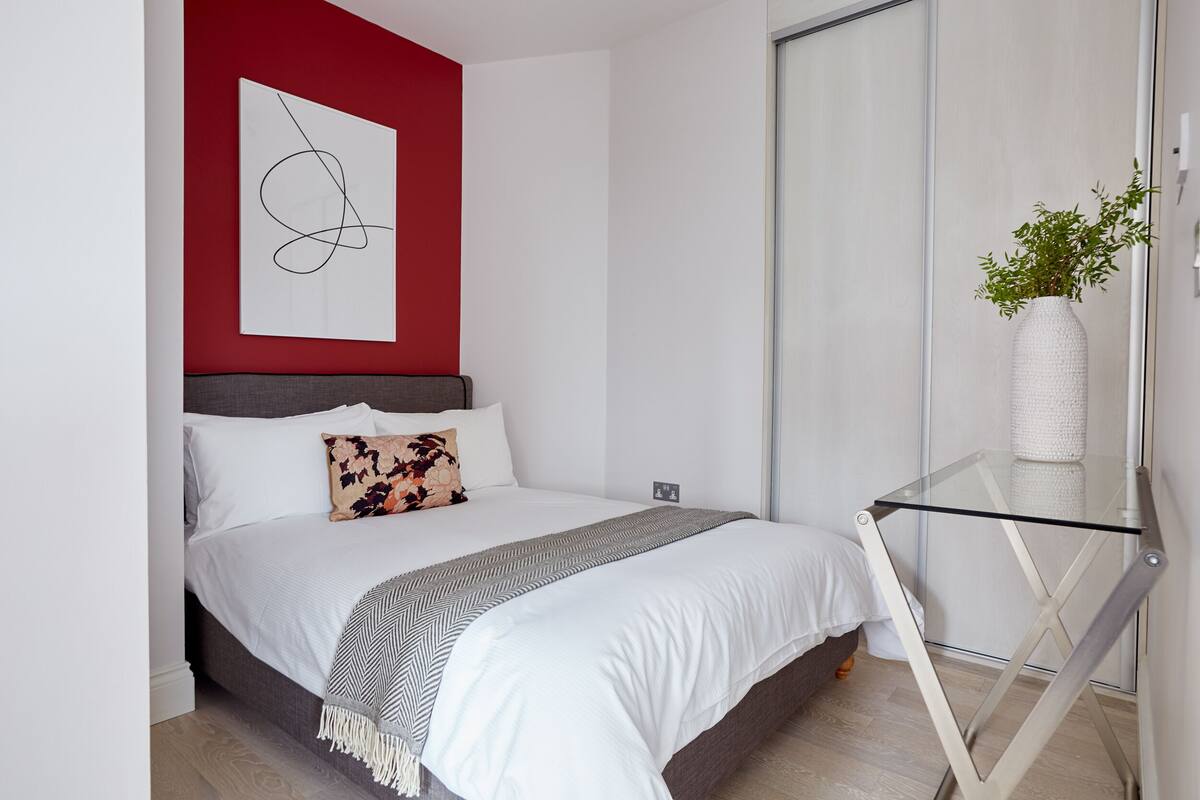 Ein modernes Schlafzimmer mit Bett, Glastisch und Pflanze.