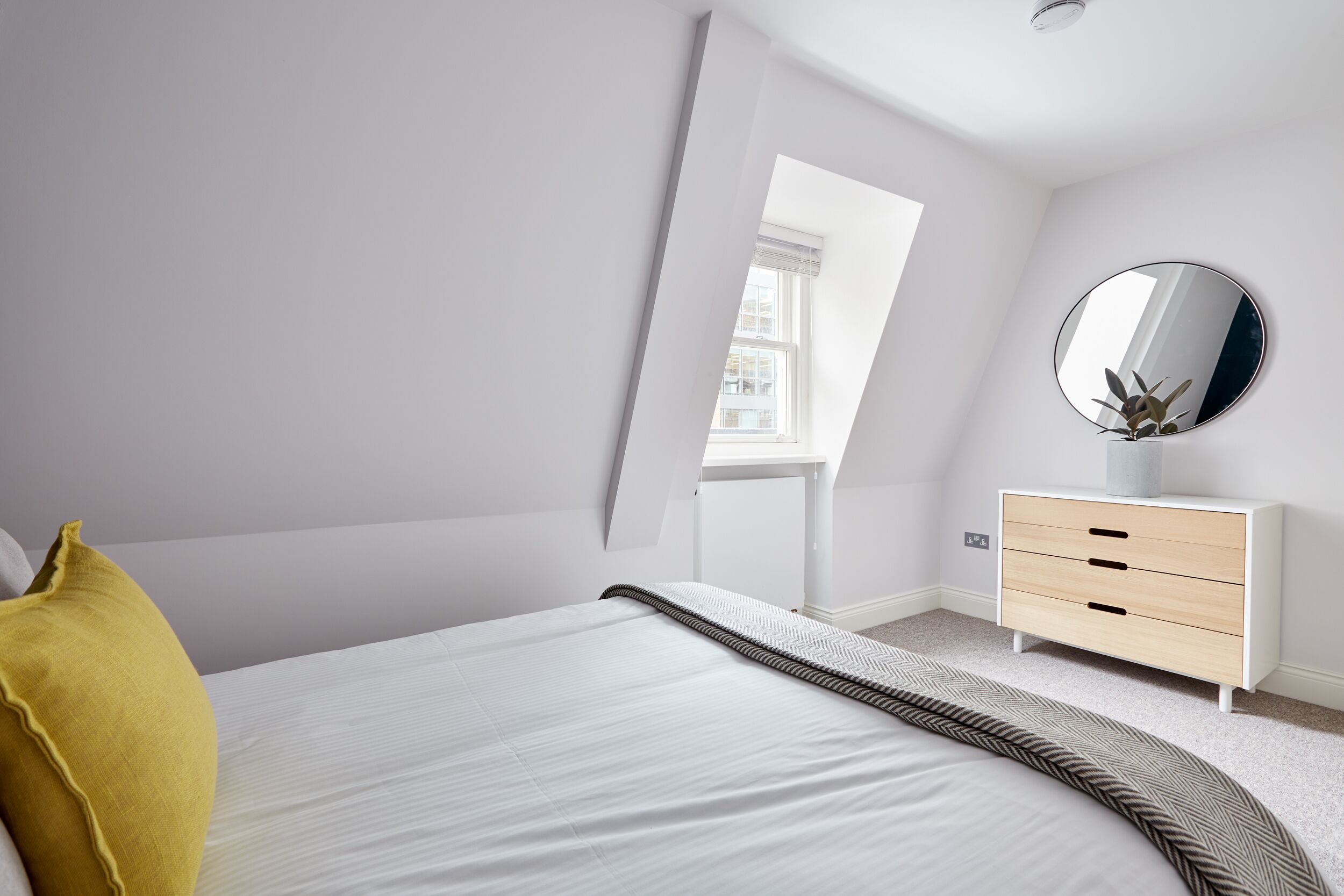 A bedroom with a bed, a bedside table, a mirror, and a window.