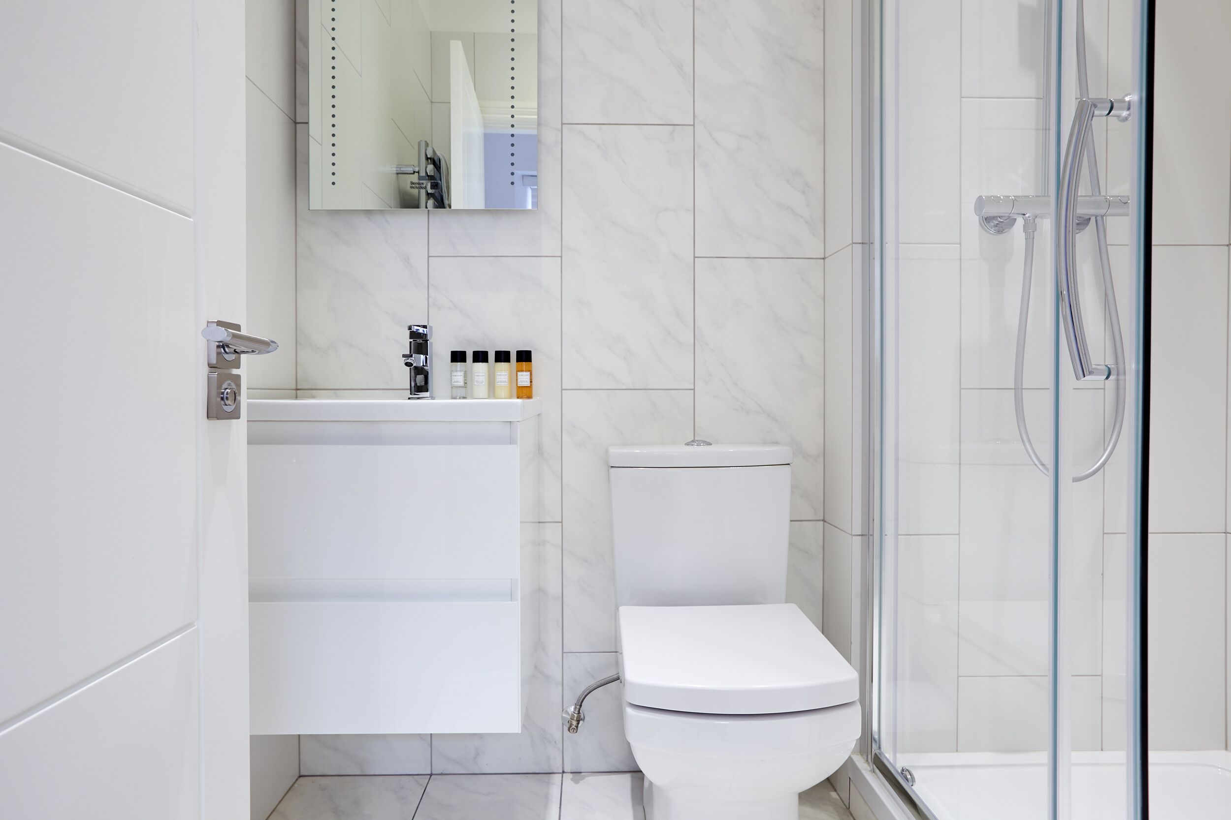 A modern bathroom with a toilet, a glass-enclosed shower, and a vanity with toiletries.