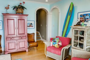 Una habitación con un armario rosa, sillas de mimbre, una tabla de surf y un cuadro con motivos playeros.