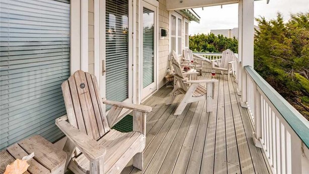 Una terraza de madera con sillas Adirondack y una mesa, con vistas a un paisaje verde.