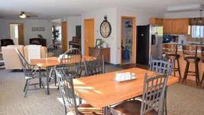 Un vaste espace de vie comprenant un coin repas avec une table et des chaises, une cuisine avec des meubles en bois et une grande horloge murale.