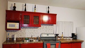 Une cuisine avec des placards rouges, un four à micro-ondes, une cuisinière et une machine à café.