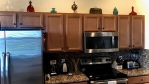 Una cocina con armarios de madera, un refrigerador de acero inoxidable, un microondas, una estufa y diversos electrodomésticos.