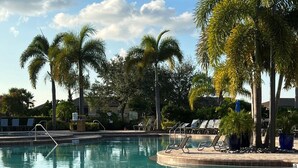 Una piscina con sillones de descanso y palmeras.