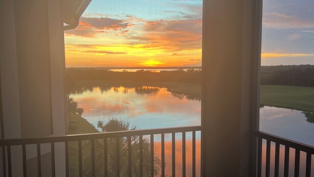 Un balcón con vistas a un atardecer sobre el agua, una silla y una mesa.