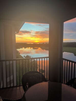 A balcony with a view of a sunset over a body of water, a chair, and a table. - TOP FLOOR CORNER CONDO (Bradenton)