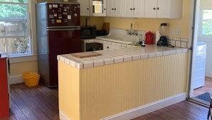 A kitchen with white cabinets, a central island, a refrigerator, a microwave, a sink, and a window. - Cozy Victorian Farmhouse in walking distance to the village of Mendocino! (Mendocino)