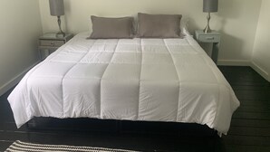 A neatly made bed with a white duvet and two pillows, flanked by two bedside tables with lamps, in a room with plain walls and a dark floor. - Cozy Victorian Farmhouse in walking distance to the village of Mendocino! (Mendocino)