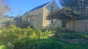 A house with a sloped roof, a front porch, and a fenced backyard with a garden. - Cozy Victorian Farmhouse in walking distance to the village of Mendocino! (Mendocino)
