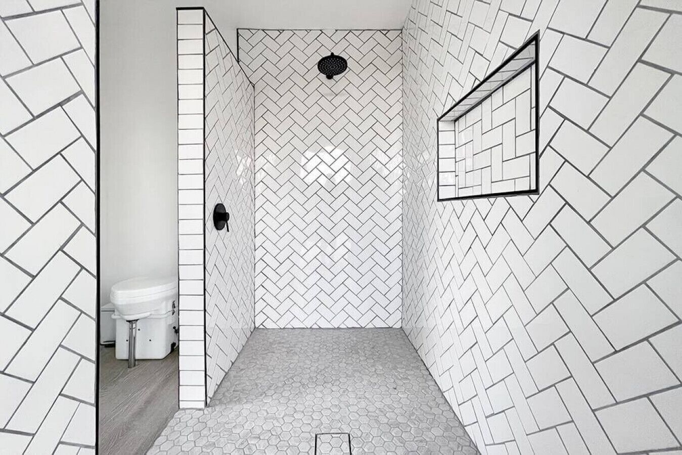 Casa de banho com padrão de mosaicos em padrão de losango, sanita e zona de duche com design de mosaicos semelhante.