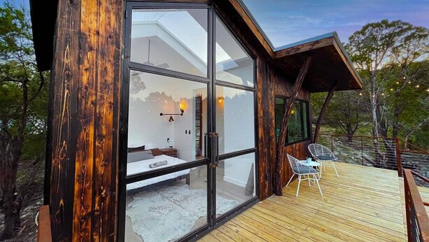 Una cabaña moderna con un amplio ventanal, una terraza de madera y vistas del paisaje circundante.