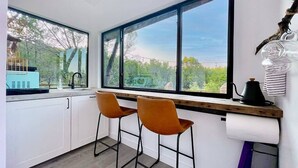 Una cocina moderna con dos taburetes tipo bar, un ventanal con vistas a la vegetación y una cafetera sobre la encimera.