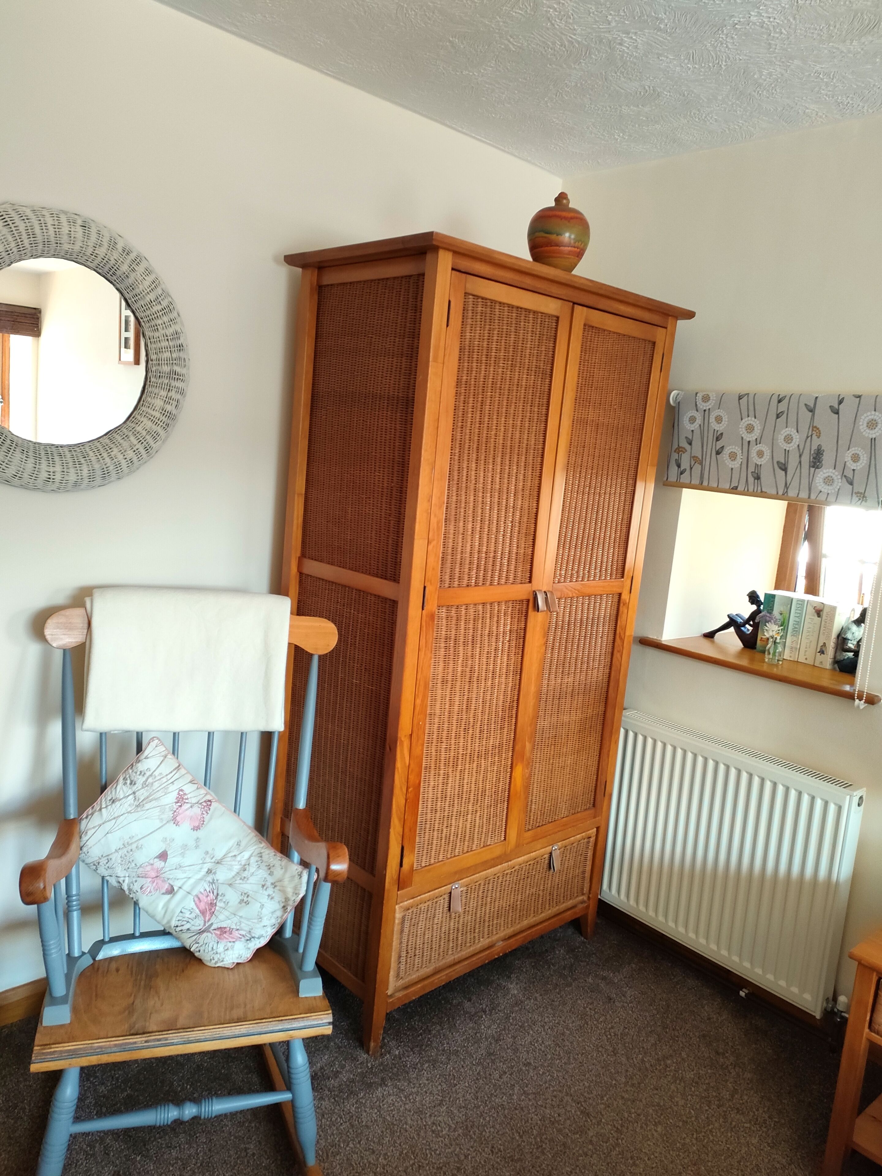Ein Zimmer mit einem Holzschrank, einem blauen Stuhl mit Blumenkissen, einem runden Spiegel und einer Heizung.
