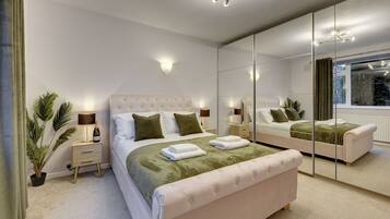 A modern bedroom with a large mirror, a bed with green and white bedding, a nightstand with a lamp, and a potted plant.