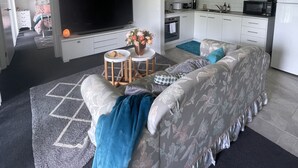 Un salon moderne avec un grand téléviseur à écran plat, un canapé et une petite table ronde agrémentée d’un vase de fleurs.