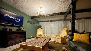 Una sala de estar con una mesa de centro de madera, dos sillones, un sofá, un televisor y una araña.
