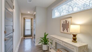 A hallway with a door, a potted plant, a wall-mounted lamp, and a framed artwork. - Modern Luxe Escape | Rooftop Views | Near Downtown (Nashville)
