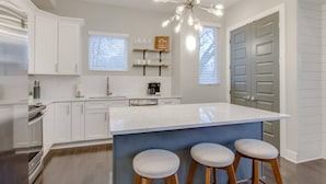 A modern kitchen with white cabinetry, a central island with stools, a chandelier, and a breakfast bar. - Modern Luxe Escape | Rooftop Views | Near Downtown (Nashville)