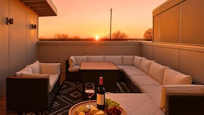 A modern outdoor seating area with a sofa and chairs, a table, and a wine bottle with grapes. - Modern Luxe Escape | Rooftop Views | Near Downtown (Nashville)