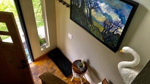 A room with a large painting of trees and a swan, a small table with a vase, and a door leading outside.