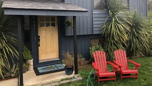 A modern house with a dark exterior, a wooden front door, and a small porch. There are two red Adirondack chairs on the grass in front.