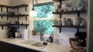 A kitchen with white countertops, a double sink, and wooden shelves holding dishes and cups.