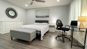 A bedroom with a bed, a desk with a chair, a desk lamp, a painting on the wall, and a mirror on the wall.