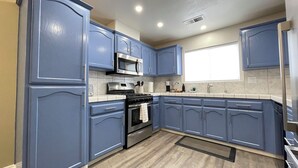 A modern kitchen with blue cabinets, stainless steel appliances, and a tiled backsplash.