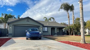 A modern two-story house with a garage, a driveway, and a well-maintained lawn with palm trees.