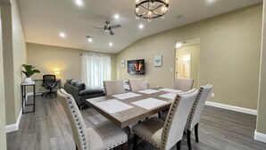 A conference room with a large table, chairs, a ceiling fan, recessed lighting, a TV, and a potted plant.