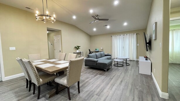 A spacious living area with a dining table, chairs, a sofa, and a TV mounted on the wall.