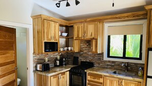 Cocina compacta con armarios de madera, microondas integrado, cocina y ventana con vista a la vegetación.