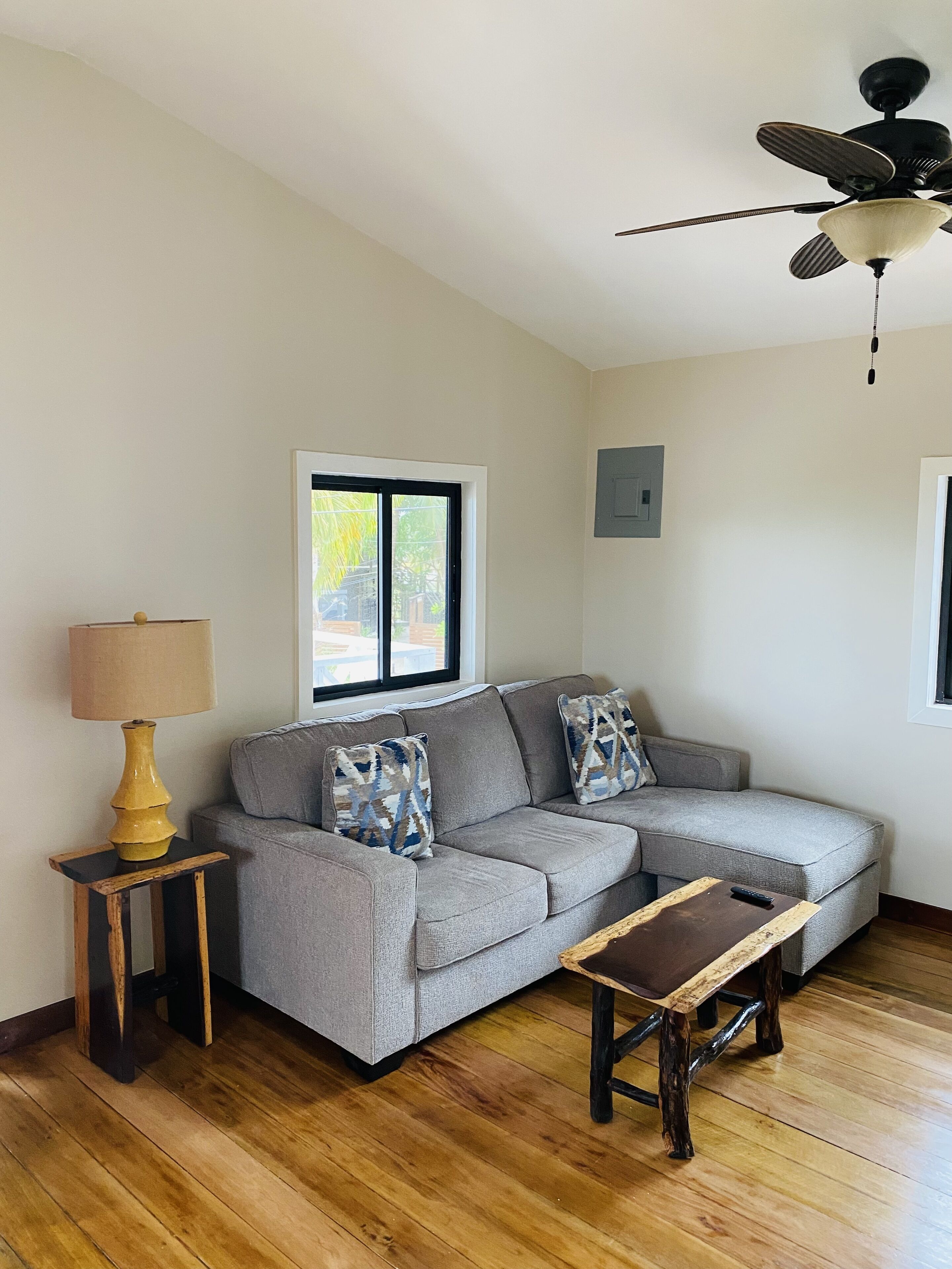 A living room with a grey sectional sofa, a wooden coffee table, a lamp, and a ceiling fan.
