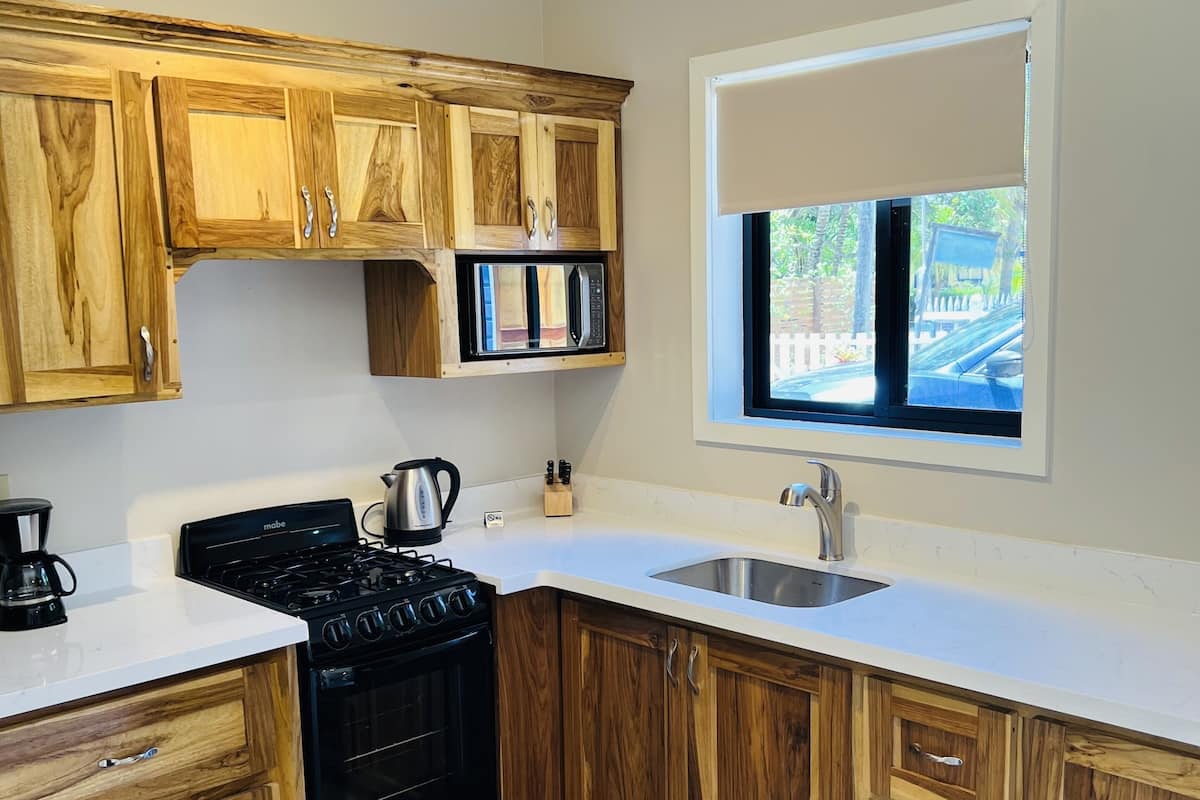 A kitchen with wooden cabinets, a black stove, a microwave, a sink, and a window with a view of the outside.