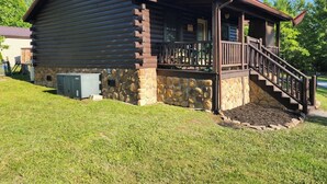 A log cabin with a stone foundation, a porch with a wooden railing, and a staircase leading to the entrance.