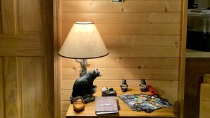 A wooden wall with a welcome sign, a bear figurine, a lamp, and a small table with various items.