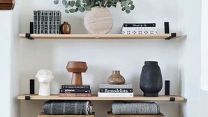 A minimalist room with two wooden stools, a potted plant, and books on shelves.