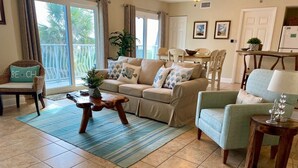 Ein Wohnzimmer mit einem beigen Sofa, einem blauen Sessel, einem Couchtisch aus Holz und einem Essbereich mit Tisch und Stühlen.